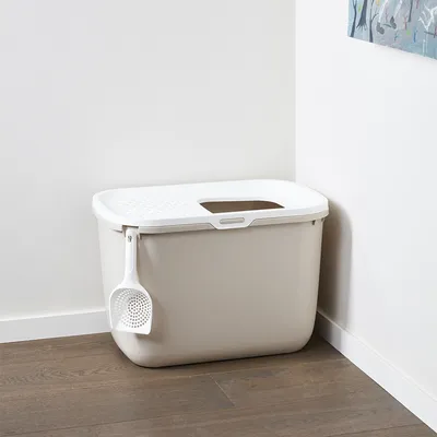 Caja de arena para gatos con tapa blanca, asa lateral y pala integrada. Apertura rectangular en la tapa para fácil acceso.