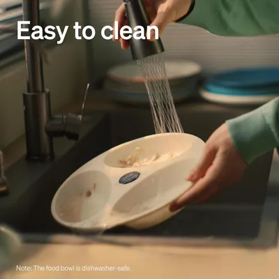 Food bowl being rinsed under a tap with text stating easy to clean and note that the food bowl is dishwasher-safe.