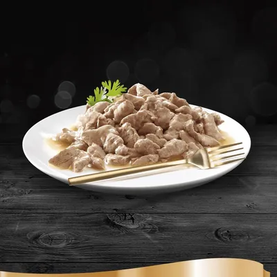 Hvid tallerken med stykker af vådfoder i sovs, pyntet med grøn krydderurt og gaffel ved siden af. Ingen synlige mærker eller tekst.