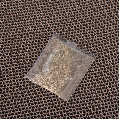 Sachet transparent contenant des herbes posé sur un carton ondulé marron, aucun texte ou marque visible.