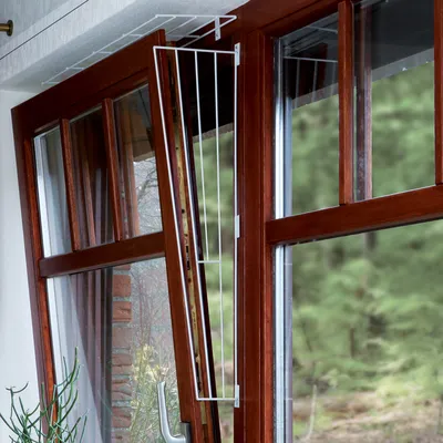 Grille de sécurité en métal blanc installée sur une fenêtre en bois ouverte, montrant la protection pour empêcher le passage à travers l’ouverture.