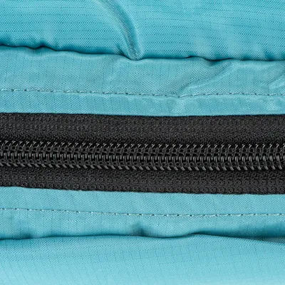 Detailní záběr na černý zip na světle modré látce, ukazuje detaily materiálu a zpracování.