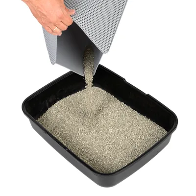 Grijze kattenbakmat waarmee kattengrit wordt teruggegoten in een zwarte kattenbak gevuld met grit. Mat heeft zichtbaar reliëfpatroon.