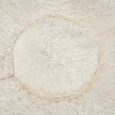 Close-up of soft, cream-coloured faux fur material with a circular pattern, showing texture and surface detail.