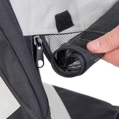 Detail van een hand die een oprolbaar gaasvenster met rits en klittenbandsluiting toont aan een zwart-grijze draagtas of bench, materiaal: textiel en gaas.