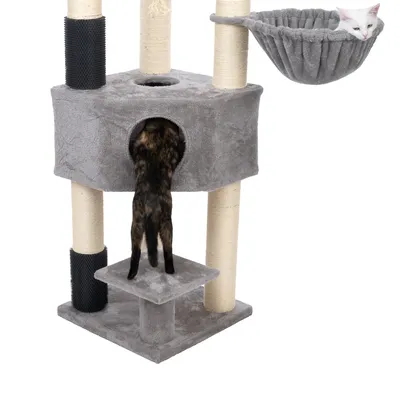Arbre à chat gris avec poteaux en sisal, niche centrale, hamac suspendu et deux chats visibles : un blanc dans le hamac, un autre entrant dans la niche.