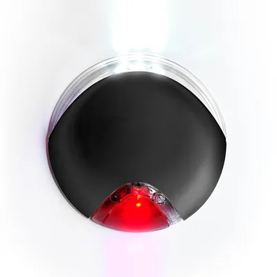 Dispositivo rotondo nero con luce LED bianca superiore e luce rossa inferiore, corpo in plastica. Nessun marchio o testo visibile.