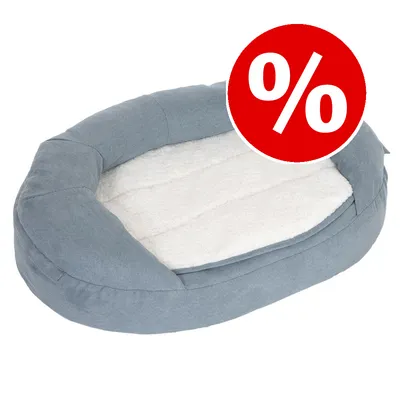 Cama ovalada para mascotas en tela gris y superficie interior blanca, con símbolo de porcentaje en círculo rojo indicando oferta o descuento visible.