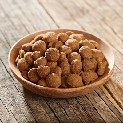 Croquettes marron en forme de boule et de cœur dans une assiette en bois, posée sur une table en bois. Aucun emballage ou marque visible.