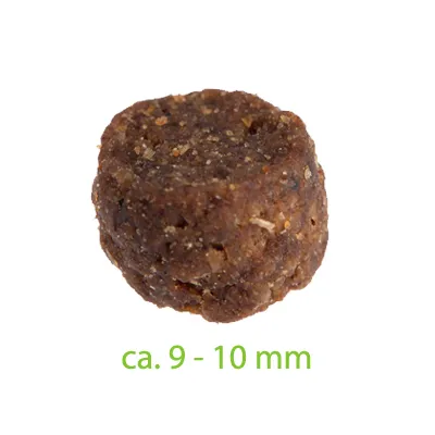 Primer plano de un trozo de alimento marrón de aproximadamente 9-10 mm, texto en verde debajo del producto.