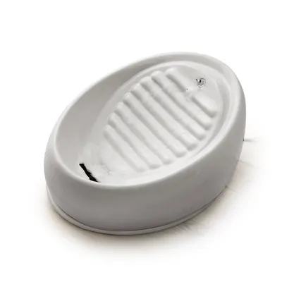 Fuente de agua para mascotas de cerámica blanca, con superficie acanalada y chorro de agua visible en el interior del recipiente.