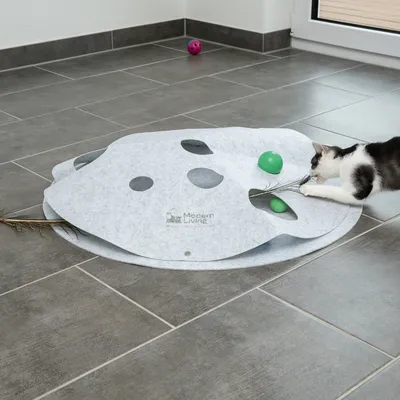 Spielmatte aus Filz mit Löchern, Marke Modern Living. Katze spielt mit grünem Ball und Federstab, weitere Spielbälle im Hintergrund.