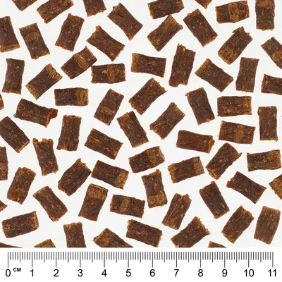 Nahaufnahme von braunen Snackstücken mit Massstab in Zentimetern unten, zeigt die Grösse der Stücke für genaue Produktbewertung.