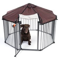 Recinto esagonale in metallo con tetto marrone e porta aperta. Cane marrone scuro seduto all’interno.