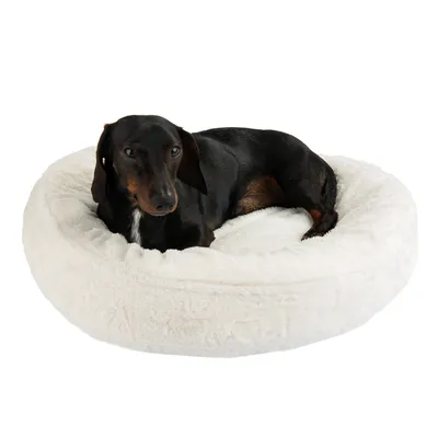 Chien noir allongé sur un coussin rond en tissu blanc, surface douce et moelleuse visible.