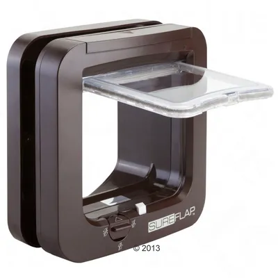 Puerta para mascotas de plástico marrón con solapa transparente y selector giratorio. Marca visible: SUREFLAP.