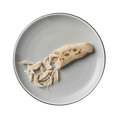 Stuk gekookte kipfilet en reepjes kip op een grijs bord, zonder verpakking of merk zichtbaar.