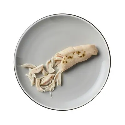 Stuk gekookte kipfilet en reepjes kip op een grijs bord, zonder verpakking of merk zichtbaar.