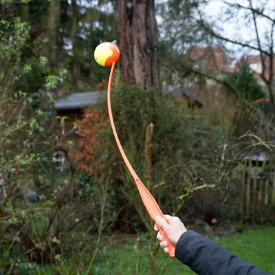 Vrhací rameno z oranžového plastu se žluto-oranžovým míčkem, vhodné pro házení míčků venku.