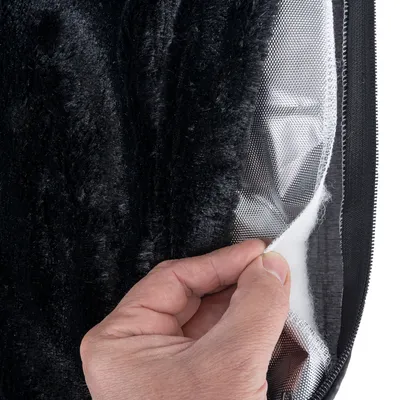 Gros plan sur une main soulevant la housse d’un coussin pour animaux, montrant plusieurs couches de tissu : peluche noire, maille grise et rembourrage blanc.