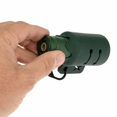 Distributeur vert de sacs en plastique avec rouleau, tenu à la main. Mousqueton noir visible pour fixation. Aucun texte ou marque apparente.