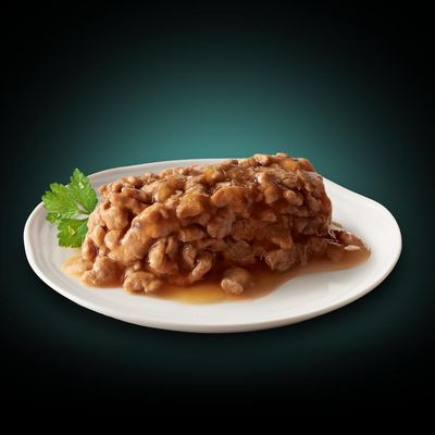 Närbild av köttbitar i sås på en vit tallrik, dekorerad med ett grönt persiljeblad.