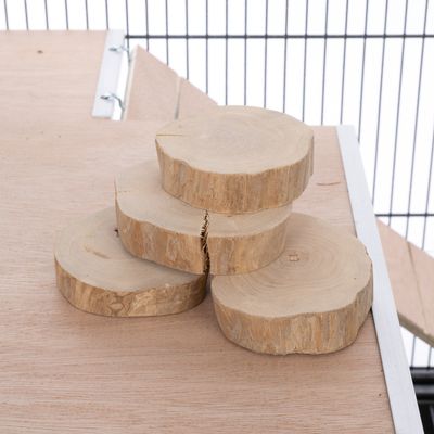 Vier runde Holzscheiben aus Naturholz, gestapelt auf einer Holzfläche. Hintergrund zeigt Metallgitter und Holzkonstruktion.