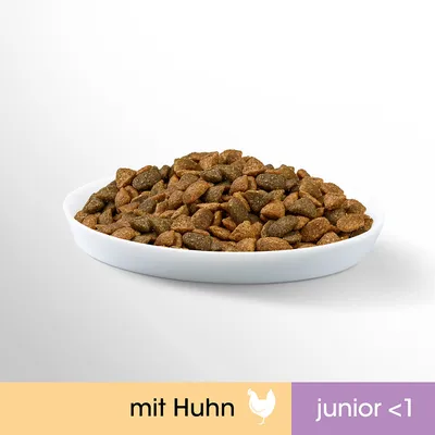 Valkoisella lautasella ruskeaa kuivaruokaa. Alareunassa teksti: mit Huhn, junior <1.