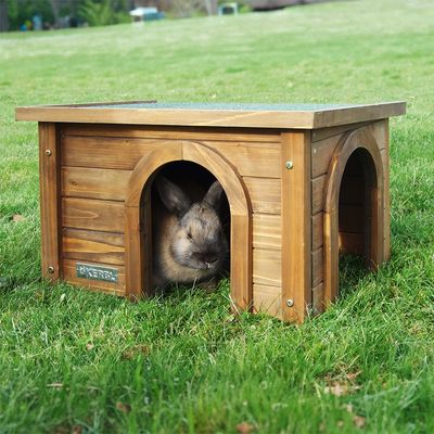 Wooden small animal house with two entrances, brand Kerbl. A rabbit sits in the entrance of the house on a green lawn.