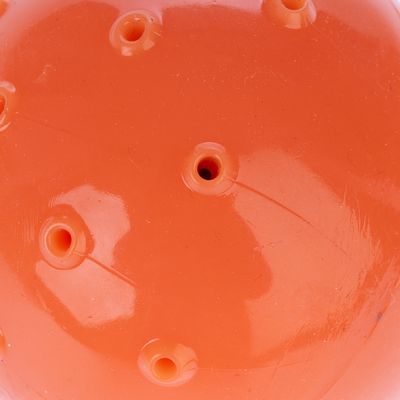 Zbliżenie na pomarańczową piłkę z tworzywa sztucznego z kilkoma małymi otworami.