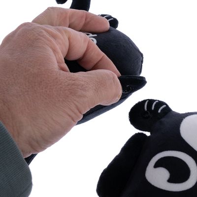 Kéz kinyitja a tépőzárat egy fekete plüssjátékon fehér részletekkel.