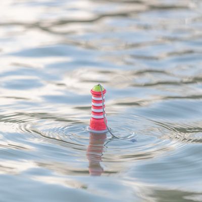 Giocattolo galleggiante a forma di faro a strisce rosse e bianche con punta verde sulla superficie dell’acqua.