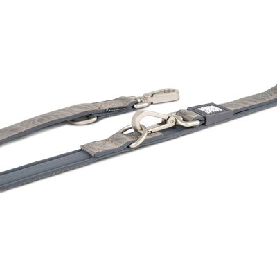 Laisse pour chien en tissu gris avec deux mousquetons métalliques et anneaux, étiquette visible avec texte blanc sur fond noir.