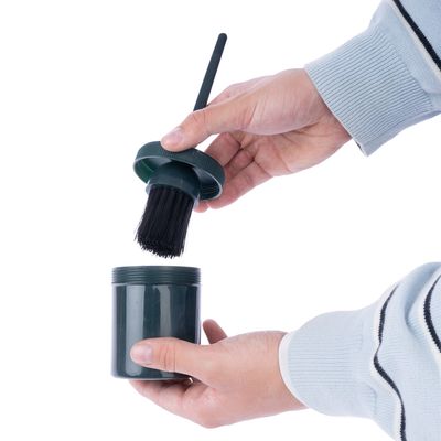 Ръка държи контейнер с капак и вграден четка, подходящ за нанасяне на течности или пасти.