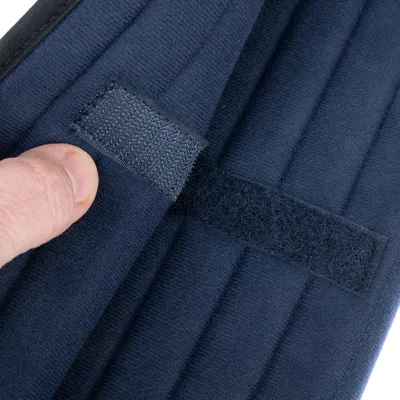Close-up van een donkerblauwe klittenbandsluiting op gewatteerde stof, geopend en vastgehouden door een hand.