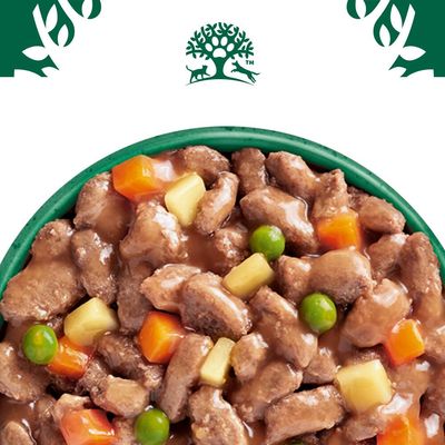 Close-up van natvoer met stukjes vlees, erwten, wortels en aardappelblokjes in saus. Bovenaan een logo met boom, hond en kat.