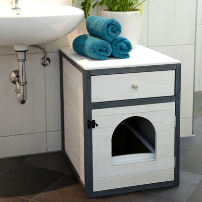 Meuble en bois blanc avec tiroir et porte à ouverture arrondie, placé sous un lavabo, trois serviettes roulées et une plante en pot posées dessus.