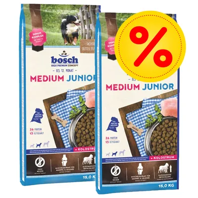 Kaksi 15 kg:n Bosch Medium Junior -koiranruokapussia, näkyvissä tekstit: 26 % proteiinia, 13 % rasvaa, ilman vehnää, kolostrum, tarjousmerkki prosenttimerkillä.
