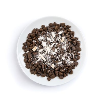 Bowl filled with dry pet food kibble topped with white powder and small chunks, showing product texture and appearance.
