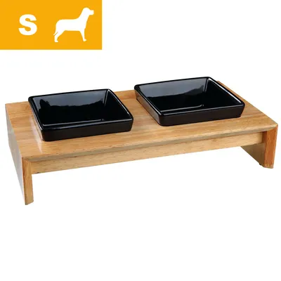 Kaksi mustaa neliönmuotoista ruokakuppia puisella korokkeella, vasemmassa yläkulmassa S-koko ja koiran siluetti. Kaksi mustaa neliönmuotoista ruokakuppia puisella korokkeella, vasemmassa yläkulmassa S-koko ja koiran siluetti.