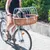 Cykelkorg av flätat trä med vitt metallgaller, lämplig för transport av liten hund. Korg monterad framtill på cykeln.