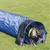 Tunnel d’agility bleu en tissu, chien de grande taille sortant du tunnel sur une pelouse. Produit destiné à l’entraînement ou au jeu pour chiens.
