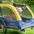 Yellow and blue dog trailer with mesh windows, brand Hafenbande. Dog sitting in the trailer on green grass.