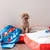 Small dog sitting on colourful cushions with Superman motifs. Product shows decorative pet bed options.