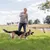 Person använder en lång leksakspinne med rep och bitrulle för att aktivera en schäferhund utomhus på gräsfält.