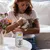 GimCat Kitten Goat Milk, woman feeding a kitten with a bottle. Product can visible on a table.