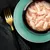 Close-up of tender chicken strips in sauce, served in a black bowl on a green plate. Golden fork and black napkin beside.