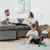 Child playing with building blocks, cat sitting on sofa next to man. In the background, cat food pack with 'Classic' label and cat image visible.