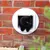 Schwarze Katze durchquert eine weisse Katzenklappe, eingebaut in eine Ziegelwand.