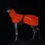 Un modello di cane nero indossa un mantello arancione brillante con motivo e striscia riflettente, fissato lateralmente con una cintura.